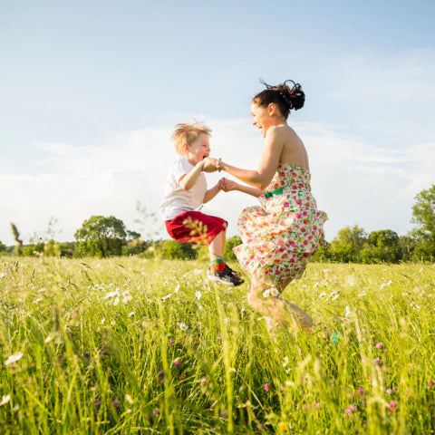 Woman and child playing in a grassy field with trees in the background