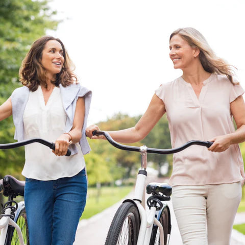 Two women walking with bicycles in a park