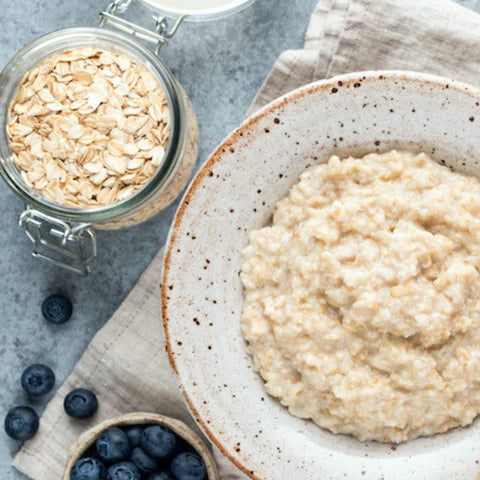 Bowl of oatmeal with a jar of oats and blueberries on a gray surface