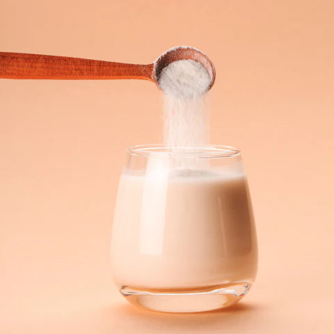 Glass of milk with a wooden spoon pouring white powder into it on a peach background