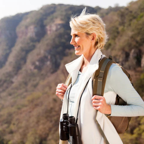 Woman with a backpack and binoculars standing in a mountainous area