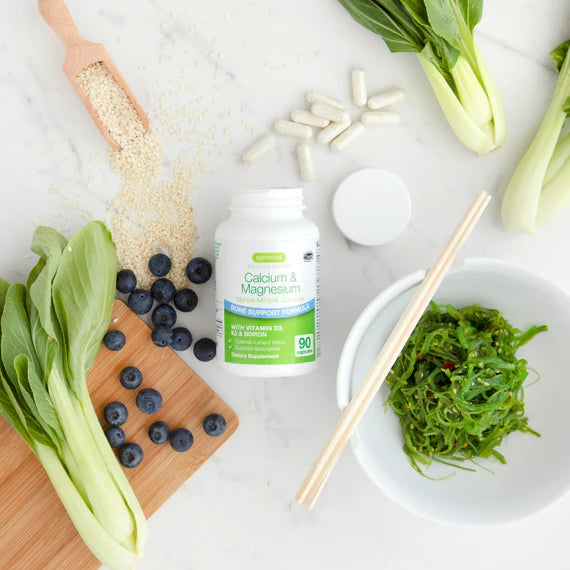 Supplement bottle labeled 'Calcium & Magnesium' surrounded by vegetables and berries on a white surface.
