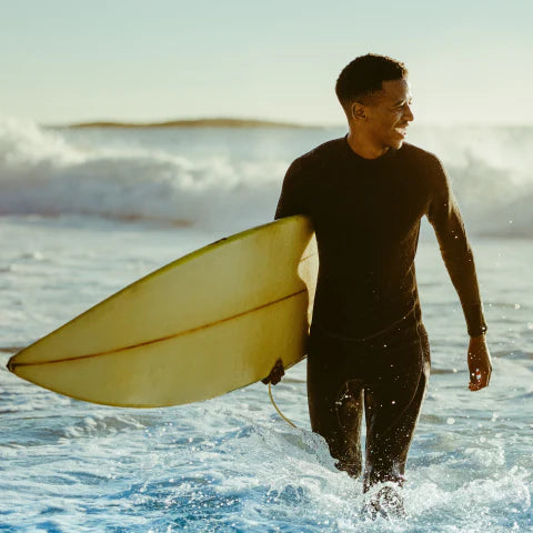 Man in a wetsuit holding a surfboard walking out of the ocean.
