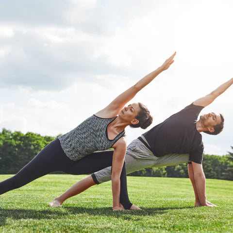 Two people practicing yoga on a grassy field with trees in the background