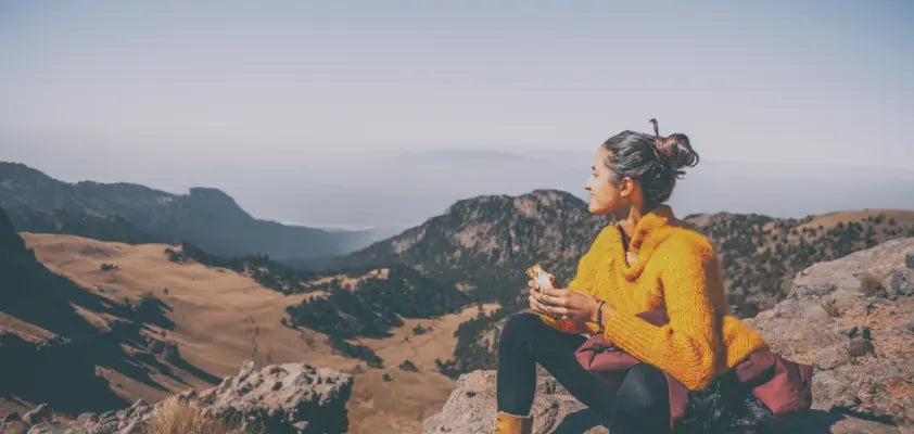Person in a yellow sweater sitting on a mountain with a scenic view